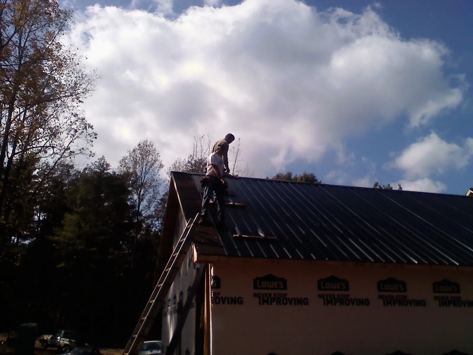 Roofer fastening dark metal panels high against a cloudy sky, from a Roof Inspection job in Haddon Heights