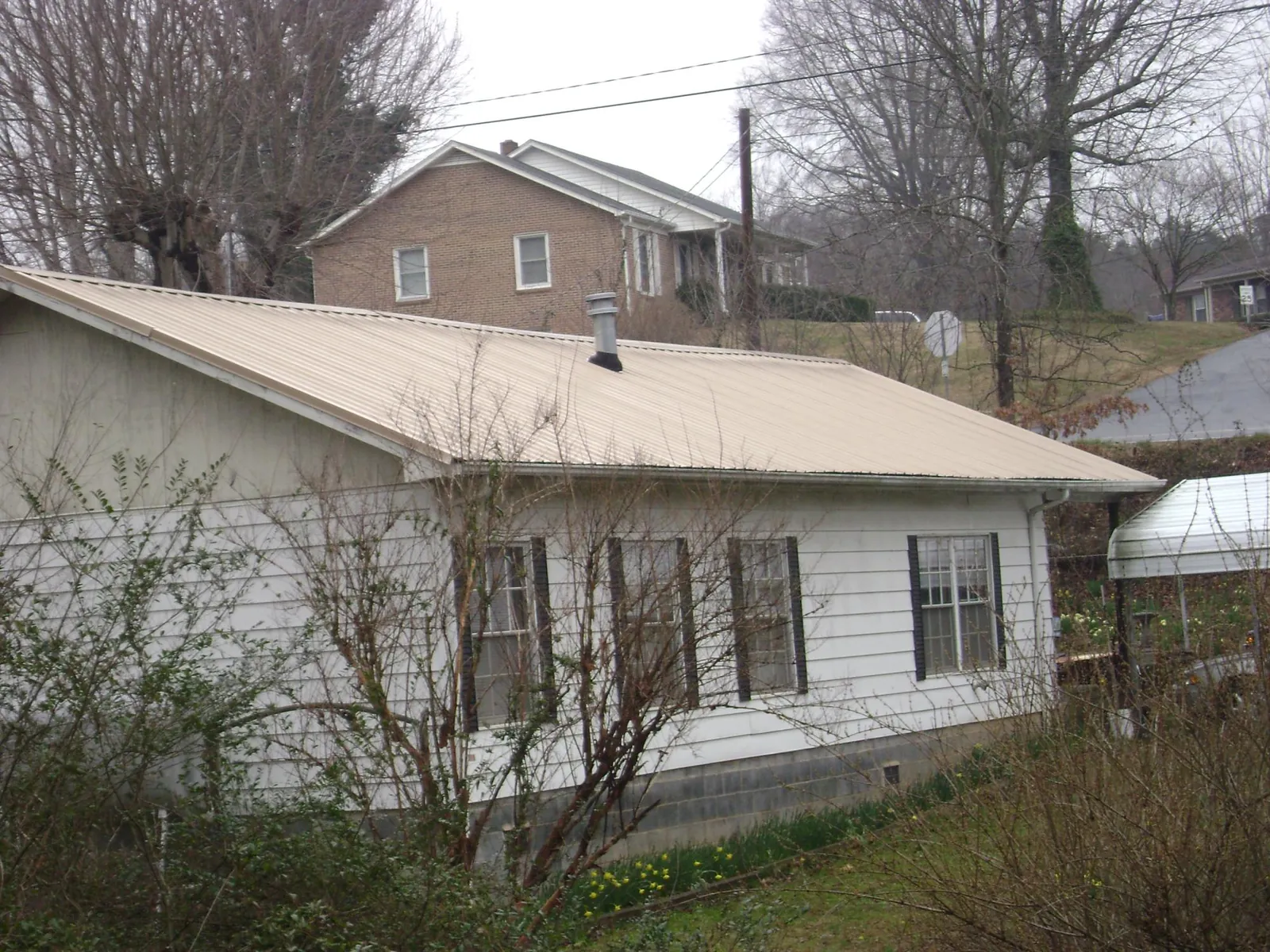 Tan metal roof on a white sided house set into a hillside — Commercial Roofing by Roofing Brothers in Haddon Heights